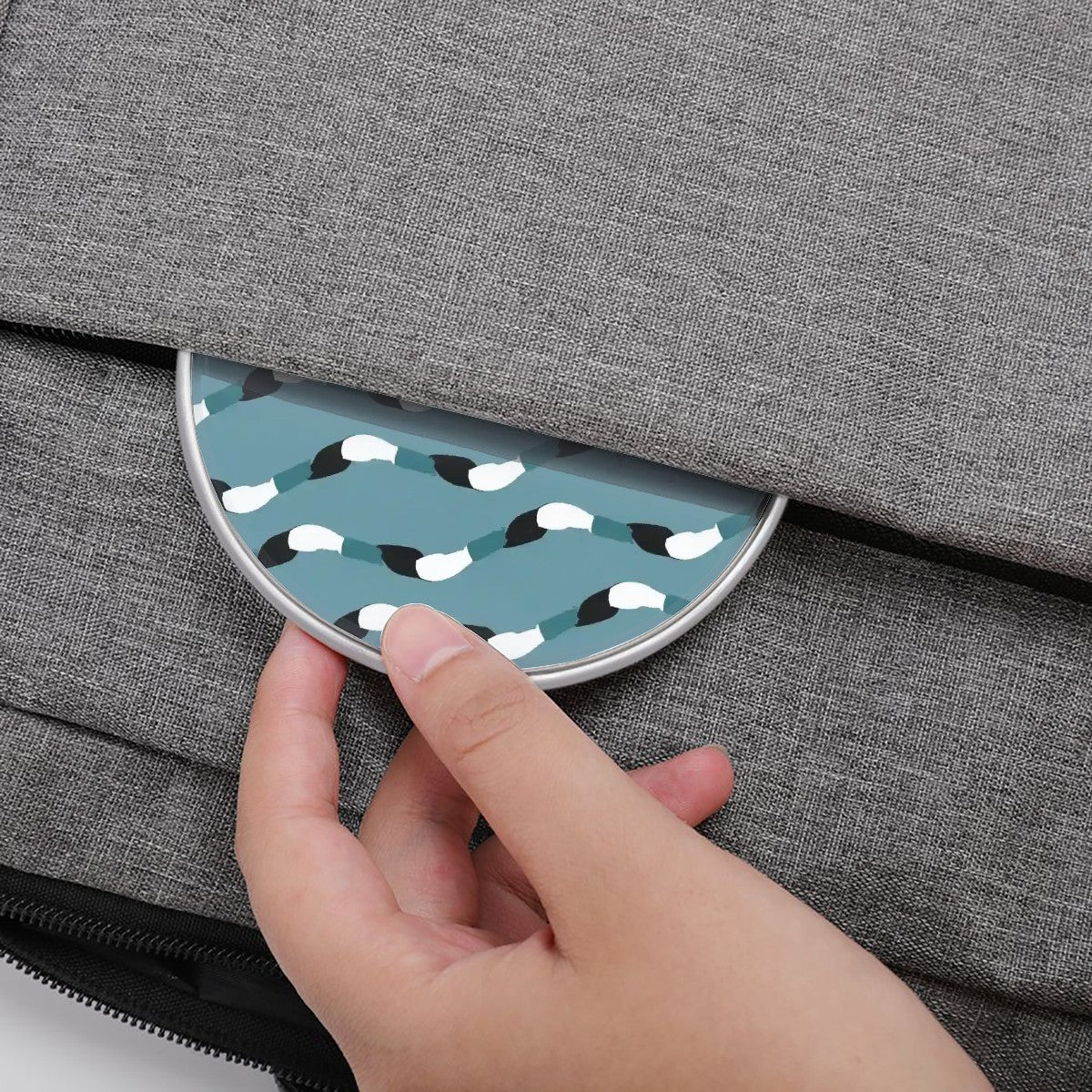 Hand opening a gray textured bag with a circular blue and white patterned pocket.