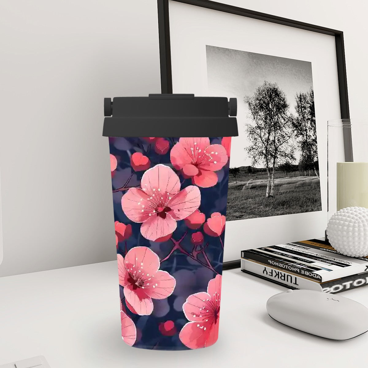 Tumbler with pink floral design on a desk with a framed picture in the background