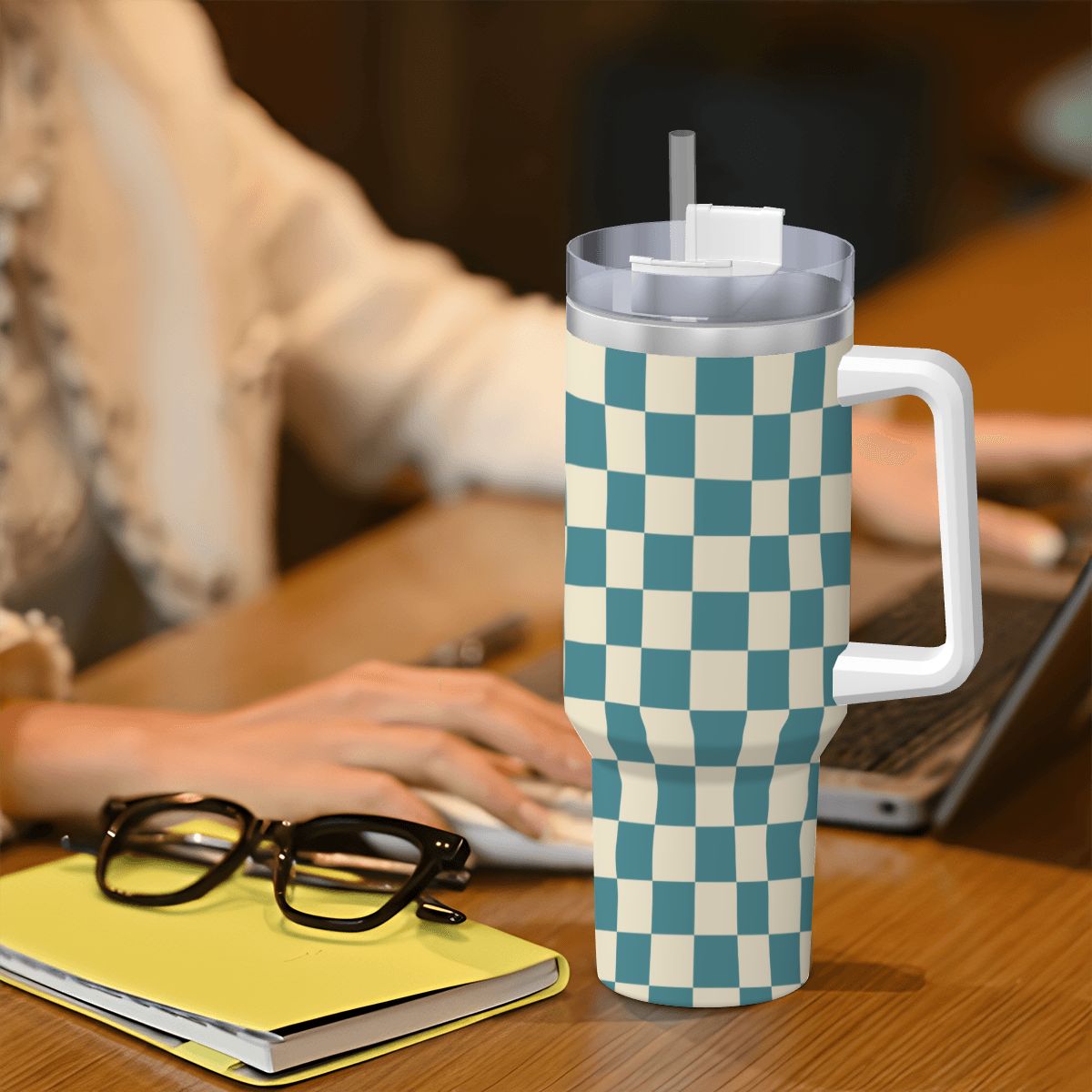 Checkered mug with handle on a desk next to glasses and a notebook