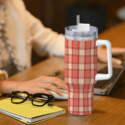 Red and white plaid mug with a straw on a desk next to a person using a laptop.
