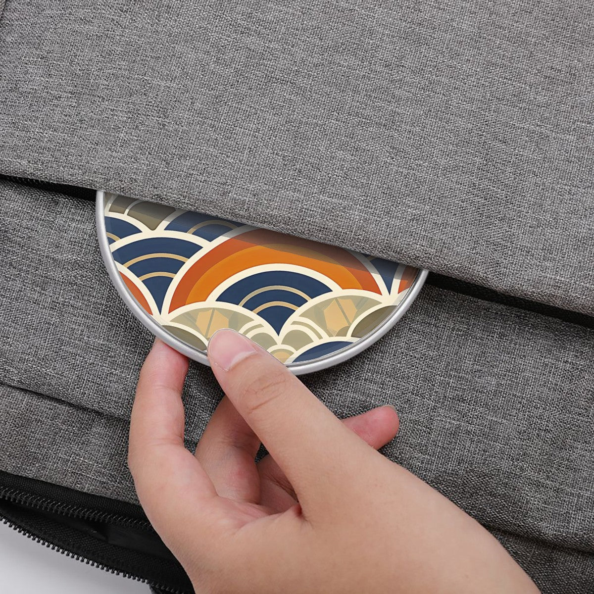 Hand placing a small round object with a colorful pattern into a gray textured bag.