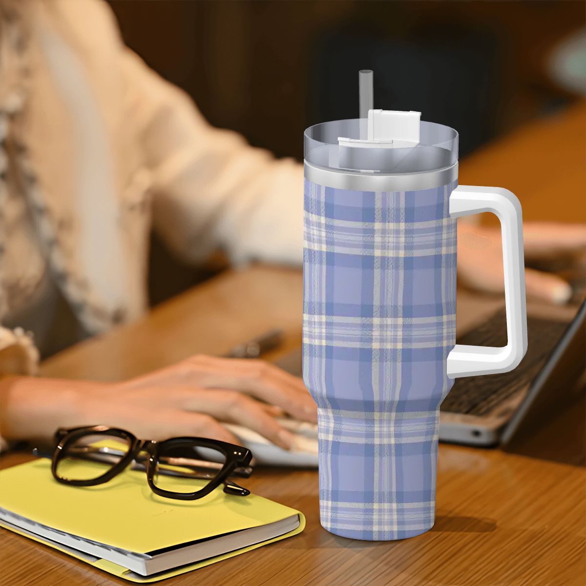 Plaid-patterned tumbler on a desk with a person using a laptop in the background