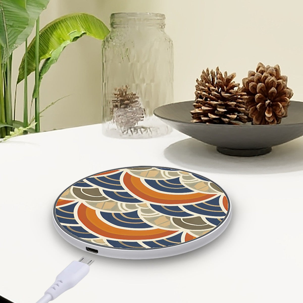 Decorative wireless charging pad with a colorful pattern on a table with a plant and decorative items.