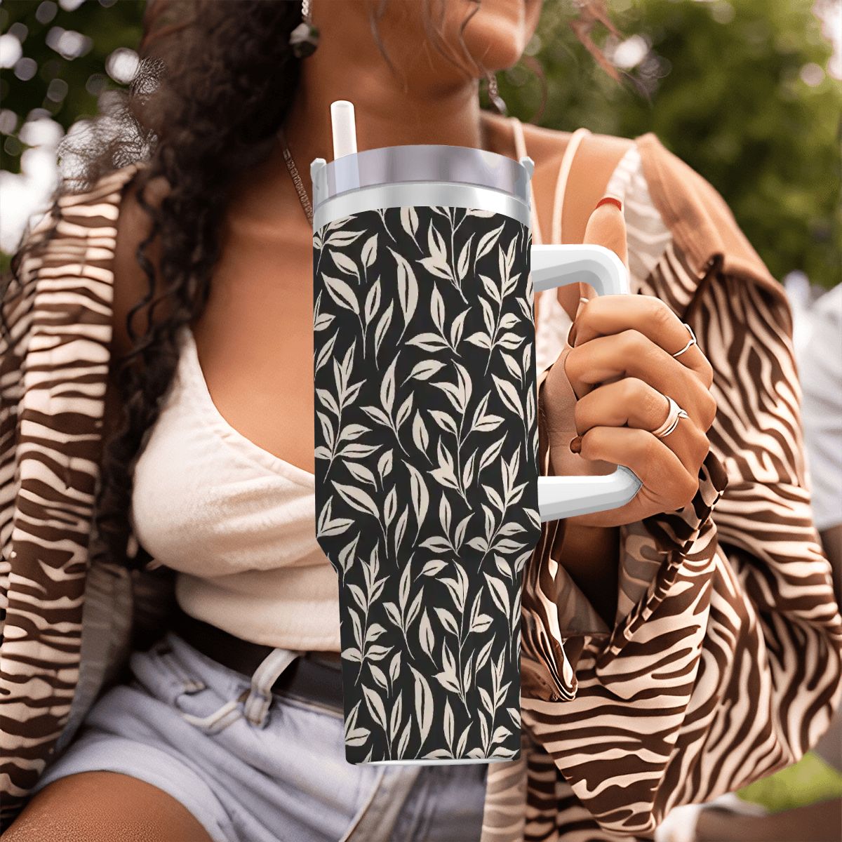 Person holding a black mug with white leaf pattern outdoors
