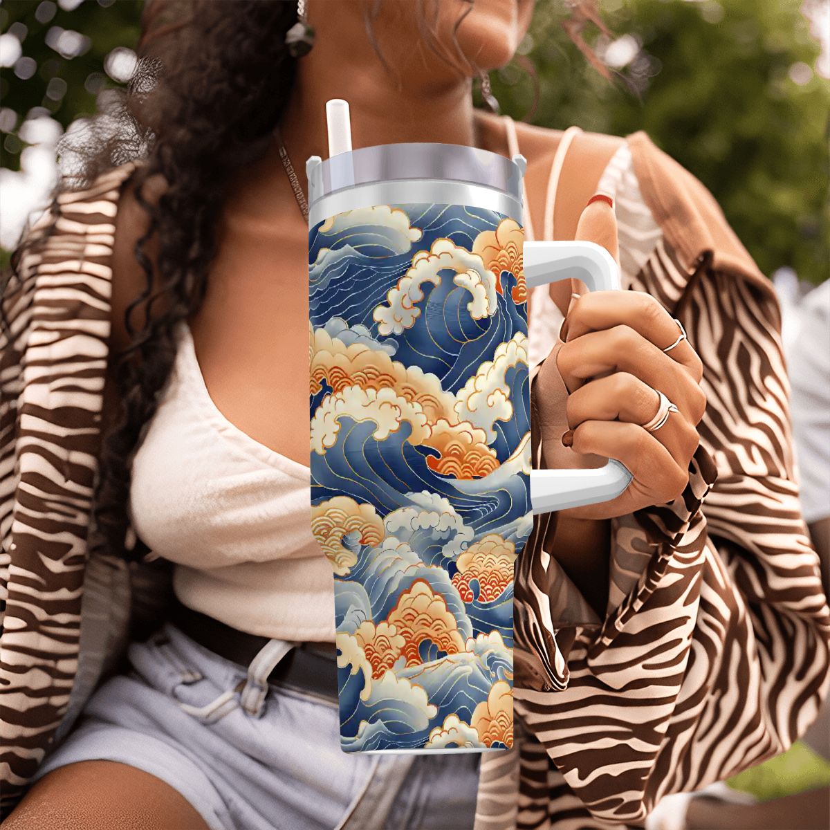 Person holding a tumbler with a wave design, wearing a zebra print jacket.