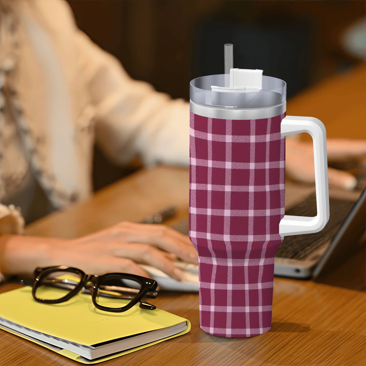 Plaid-patterned tumbler on a desk with a person using a laptop in the background
