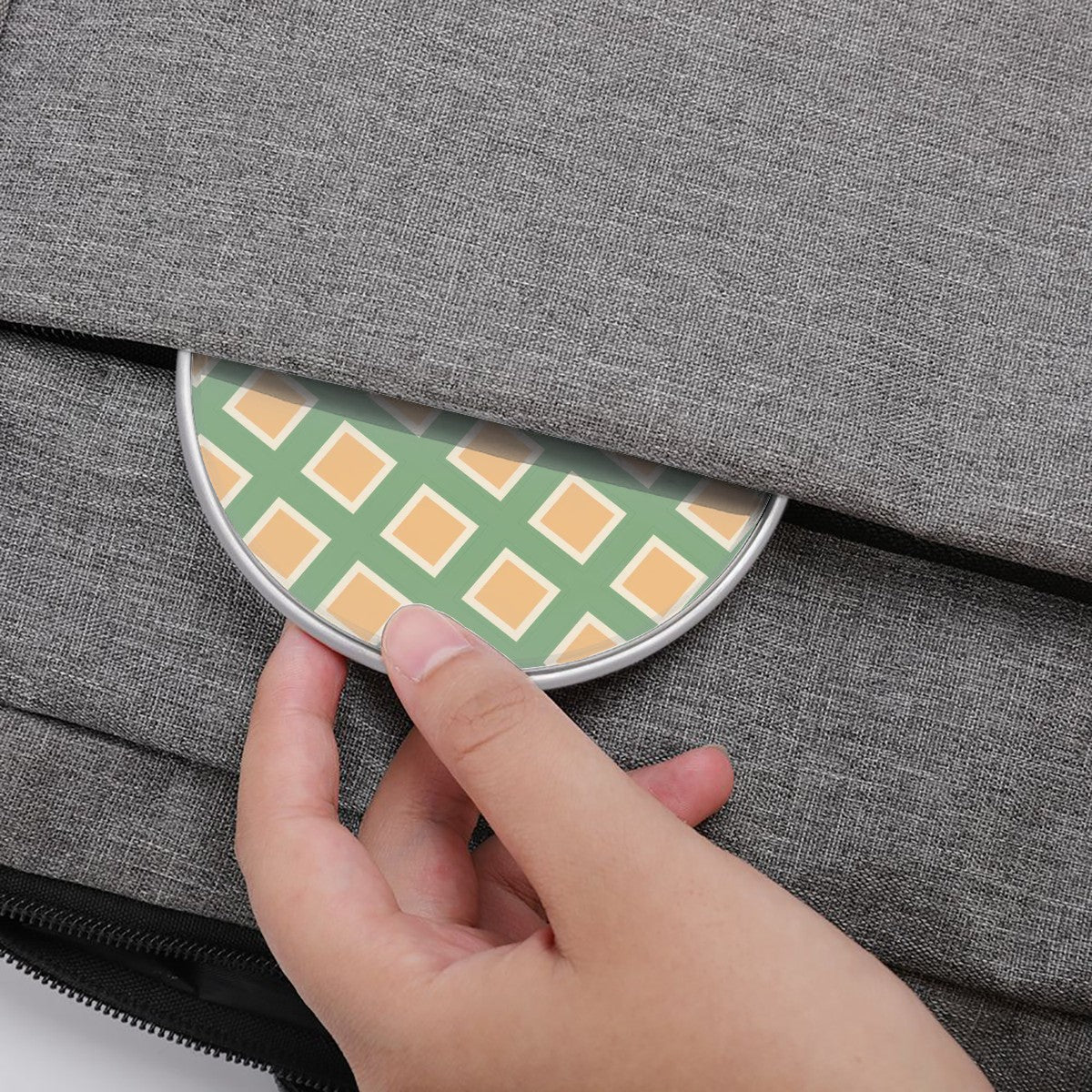 Hand placing a green and orange checkered object into a gray fabric bag.