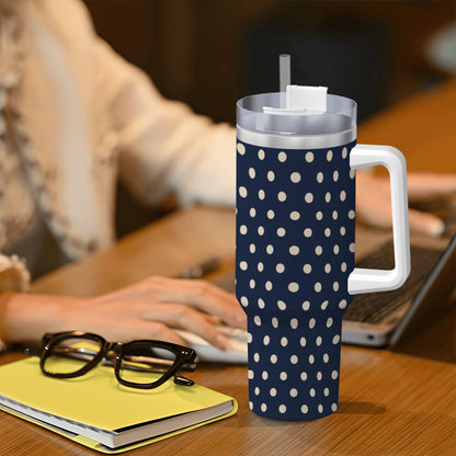 Navy blue tumbler with white polka dots on a desk with a person using a laptop.