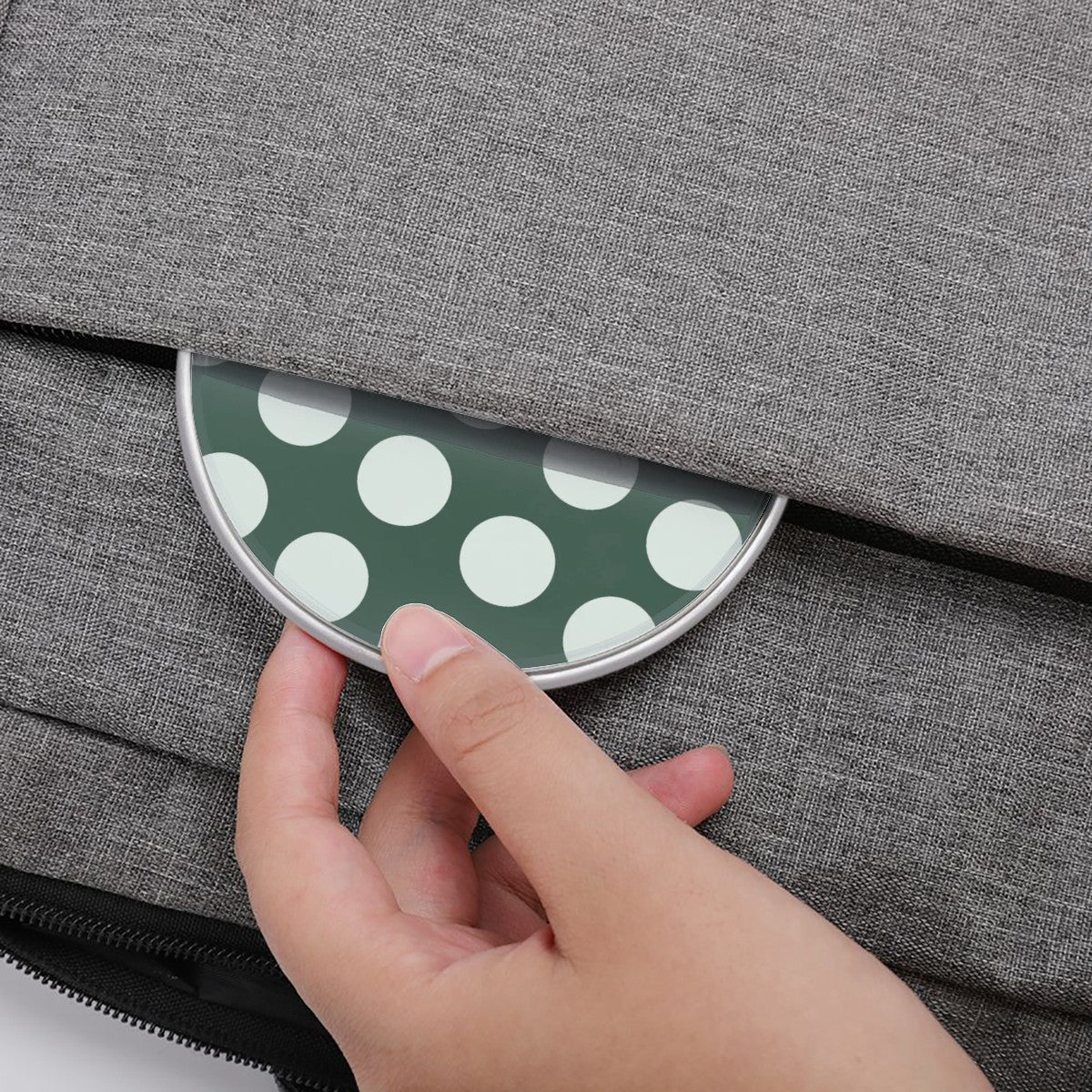 Hand placing a green polka dot item into a gray fabric bag