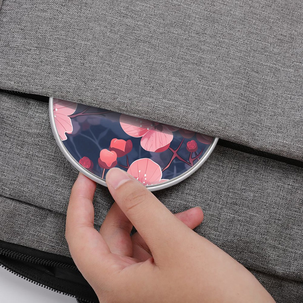 Hand placing a compact mirror with floral design into a gray bag.