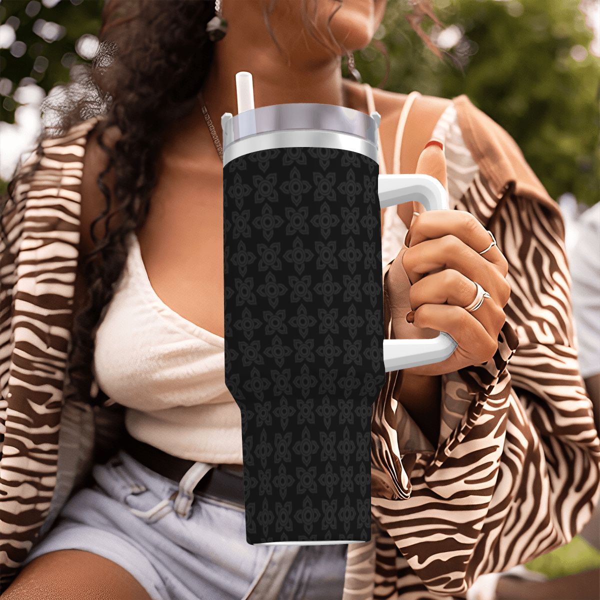 Person holding a black patterned tumbler with a blurred outdoor background