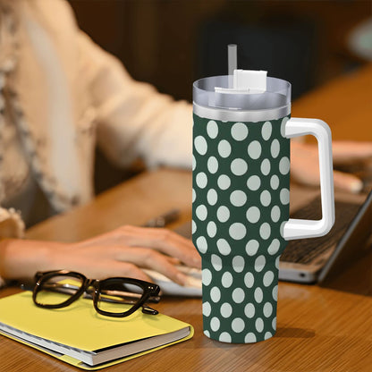 Green tumbler with white polka dots on a desk next to glasses and a notebook.