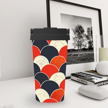 Colorful geometric-patterned travel mug on a desk with a framed black and white photo in the background.